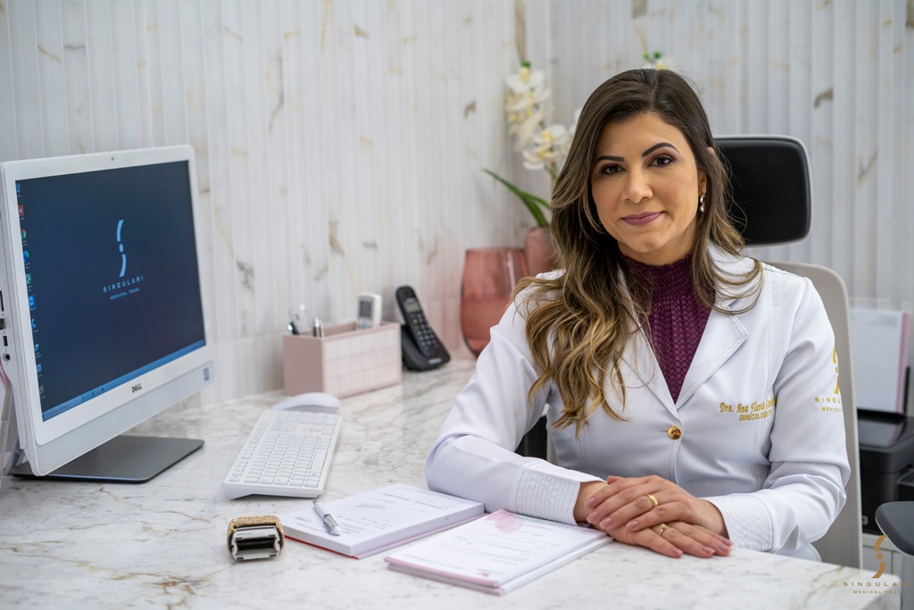 Ginecologista Ana Flávia Cavalcante de jaleco, posando sentada em seu consultório explica vantagens do laser íntimo