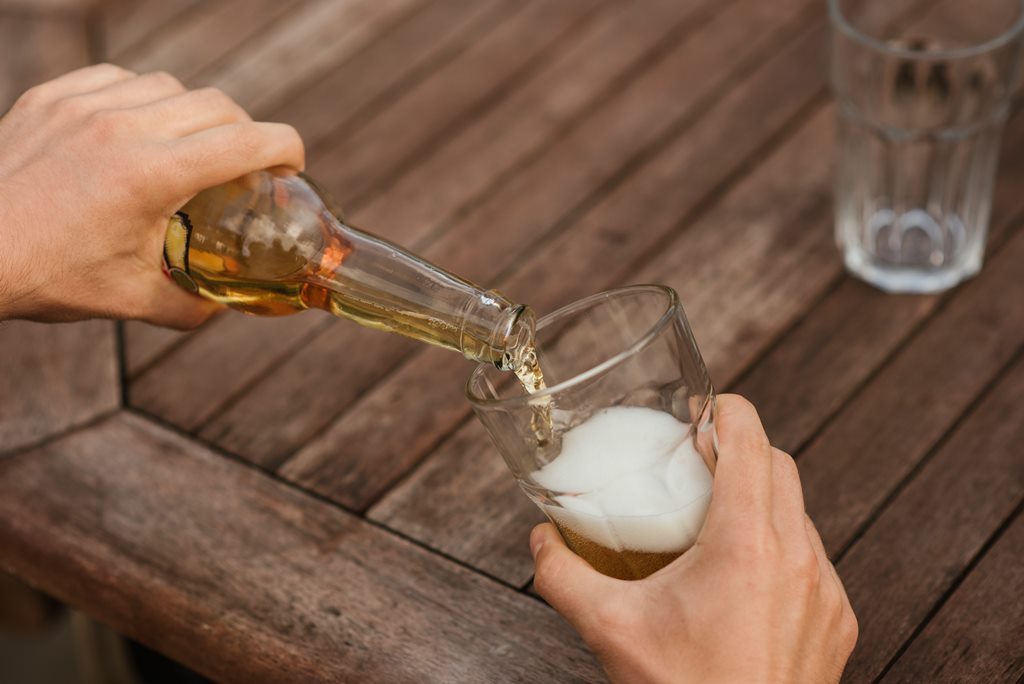 Homem despeja bebida alcoólica em copo de vidro.