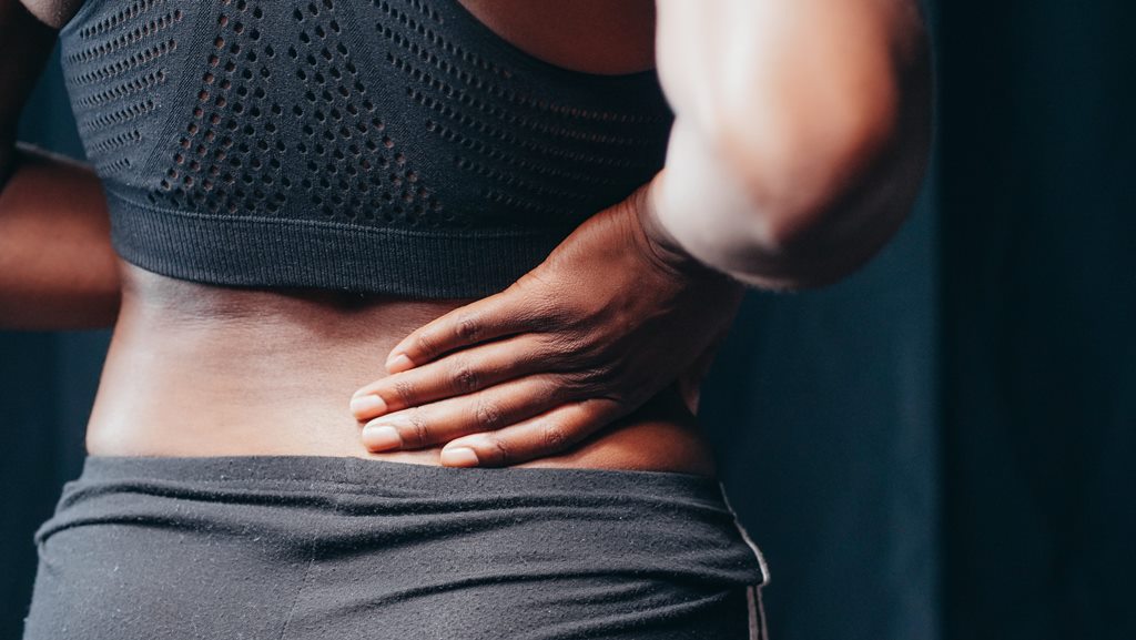 Mulher negra em roupas de academia com dor renal característica ao câncer de rim.