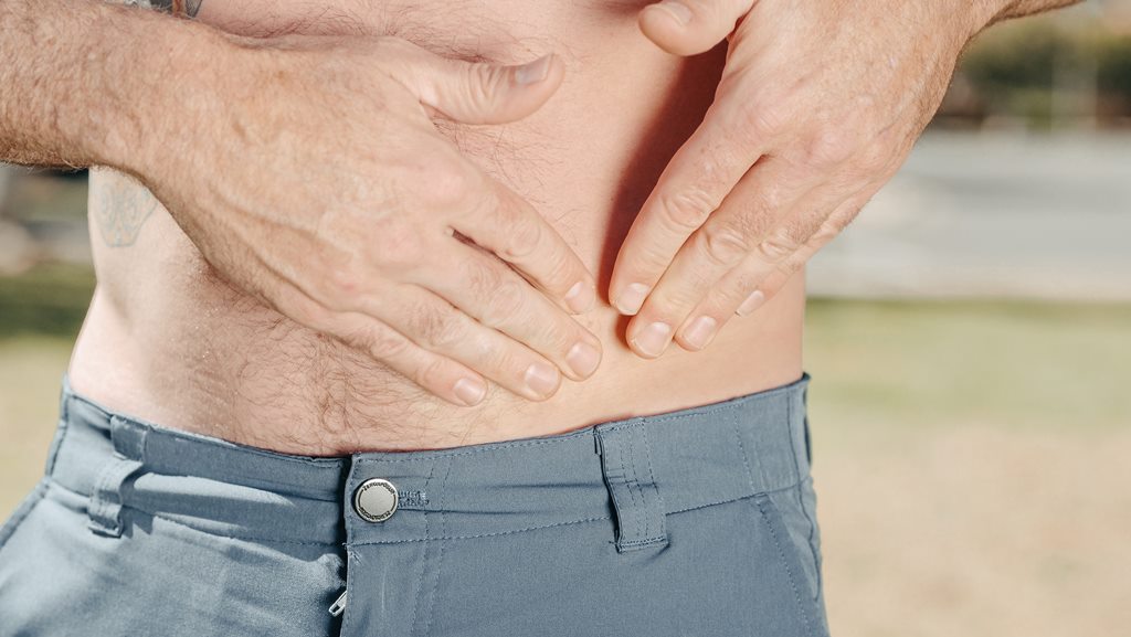 Homem sem camisa pressiona a lateral do abdome em sinal de dor na região do intestino.